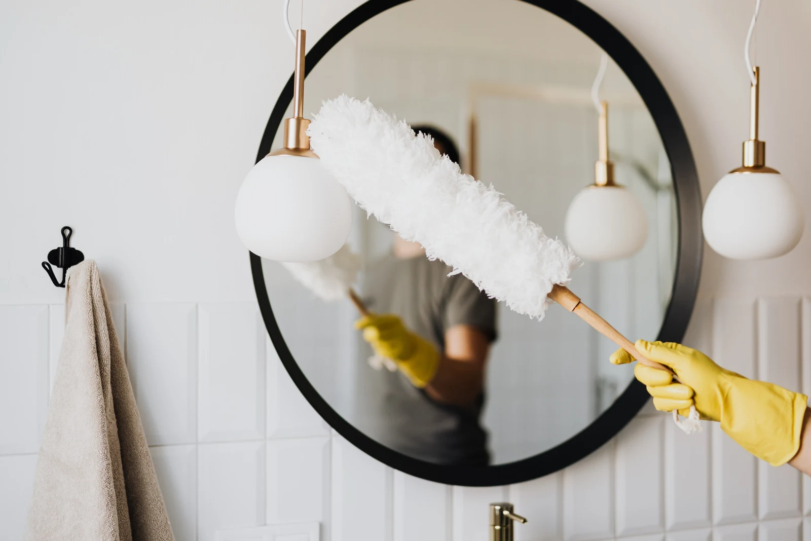 Cleaner dusting a mirror and light fixture